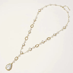 Y-shaped gold necklace with alternating geometric links, freshwater pearls, and baroque pearl pendant on cream background