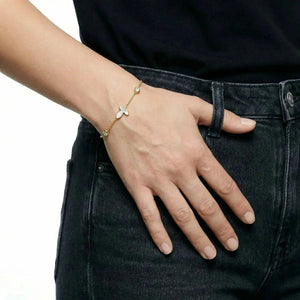 Gold chain bracelet with cross charm and crystals on wrist, worn with black jeans