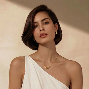 Woman wearing elegant gold necklace and hoop earrings with a white one-shoulder dress