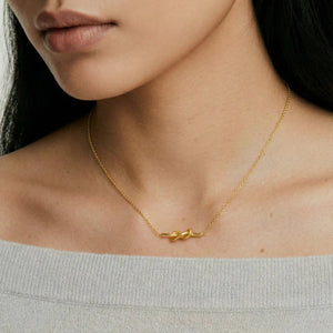 Woman wearing a delicate gold knot necklace on a fine chain, off-shoulder sweater visible