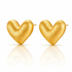 A pair of textured gold heart-shaped stud earrings on a clean white background with soft reflections below.
