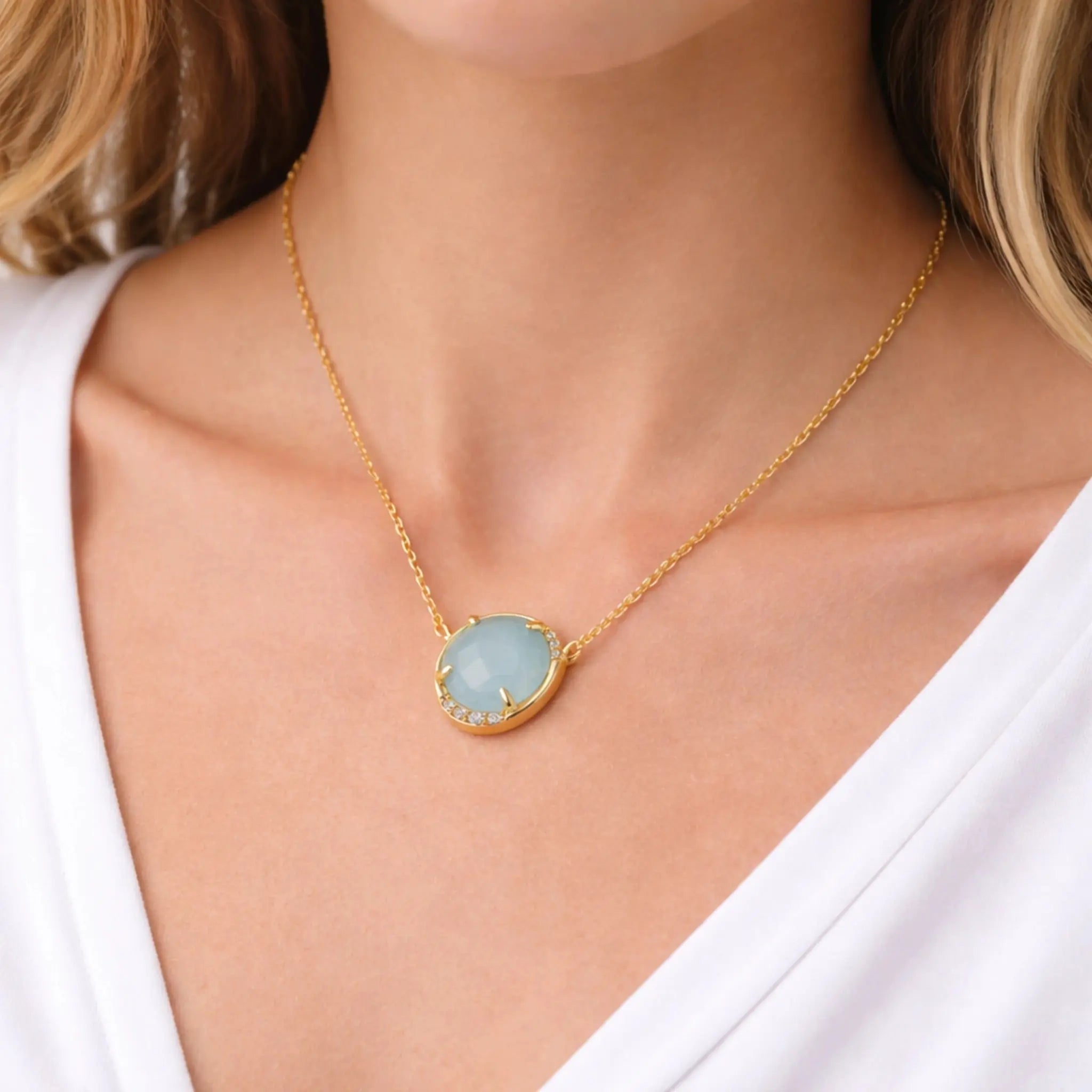 Gold oval pendant necklace with aqua gemstone and small crystals on model's neck