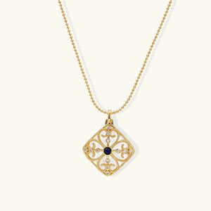 Gold necklace with a decorative pendant featuring a blue gemstone on a white background