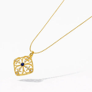 18K gold medallion necklace with blue center stone and diamond accents on white background