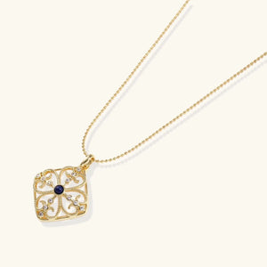 Gold necklace with a square pendant featuring a blue gemstone on a white background