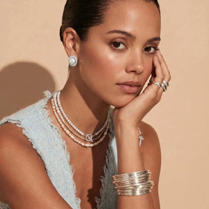Woman wearing pearl earrings, necklaces, and bracelets on a beige background