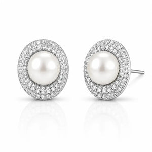 A pair of oval stud earrings featuring a central white pearl surrounded by a halo of small clear stones in a silver-toned setting, shown on a clean white background with a soft reflection below.