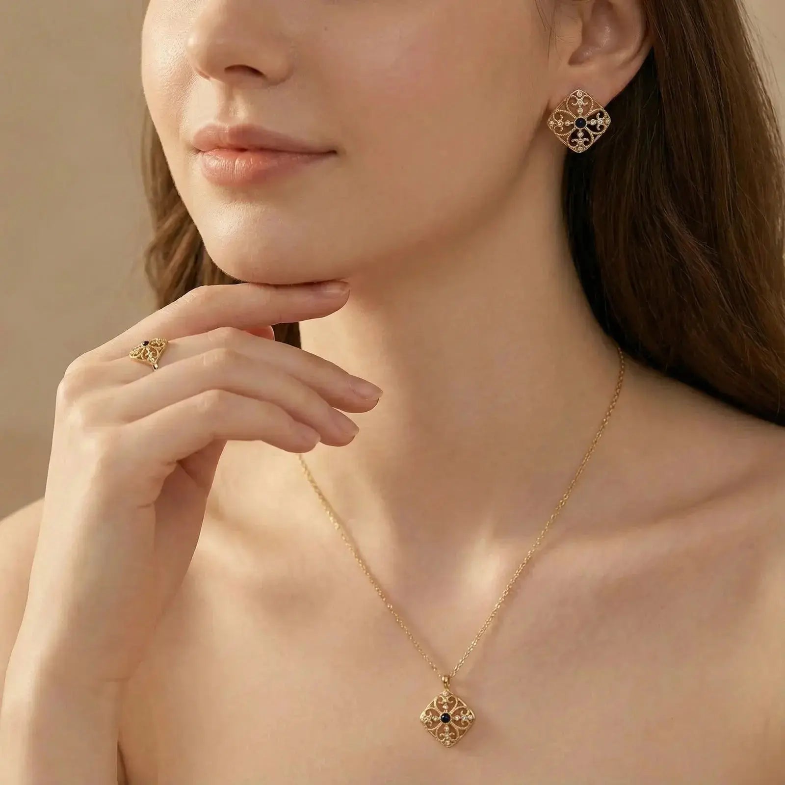 Woman wearing matching gold stud earrings, necklace, and ring with blue gemstone accents