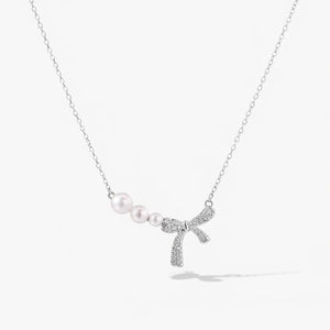 Silver necklace with three pearls and a crystal-studded bow pendant on a white background