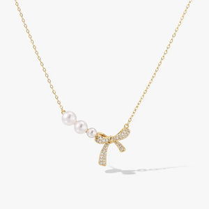 Gold necklace with three freshwater pearls and a crystal-encrusted bow pendant on white background