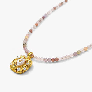 Beaded gemstone necklace with gold pendant, pearl center, and crystal accents on white background