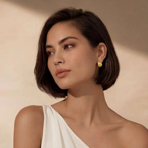 Woman wearing gold hammered huggie earrings, elegant jewelry, neutral background.