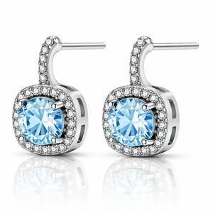 A pair of silver-toned drop earrings featuring a large round light blue gemstone in a square halo setting, surrounded by small clear stones, with post-back closures, shown on a white background with a soft reflection.