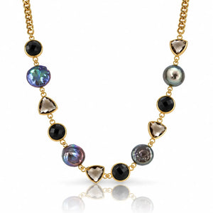 A gold chain necklace featuring alternating round black onyx beads, faceted smoky quartz triangle beads, and irregular iridescent pearl beads in gold settings, displayed on a clean white background with a soft reflection.
