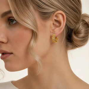 A close-up of a woman wearing a small gold hoop earring with clear stones, shown in profile against a soft cream background.