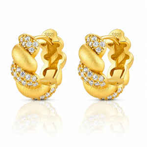 A pair of gold huggie hoop earrings with clear pavé-set round stones, shown on a white background with a soft reflection below. The inside of the earrings is stamped with 'S925' indicating sterling silver base metal.