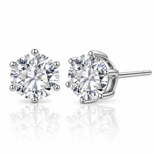A pair of round-cut diamond stud earrings in a silver four-prong setting, with one earring facing forward and the other angled to show the post and back, on a reflective white surface.