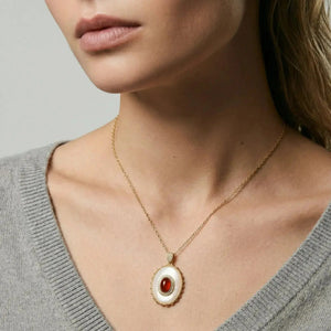 Woman wearing gold chain with oval cameo pendant featuring red gemstone center