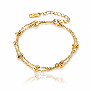 A gold double-strand chain bracelet with small polished bead accents and an adjustable lobster clasp, shown on a clean white background with a soft reflection below.
