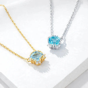 Gold and silver necklaces with blue topaz halo pendants on a white background