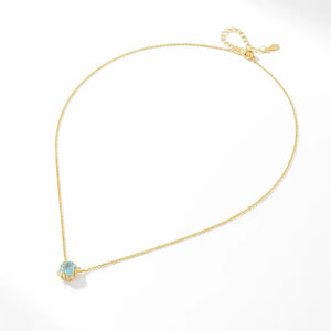 Gold plated silver necklace with a round blue topaz halo pendant on a white background