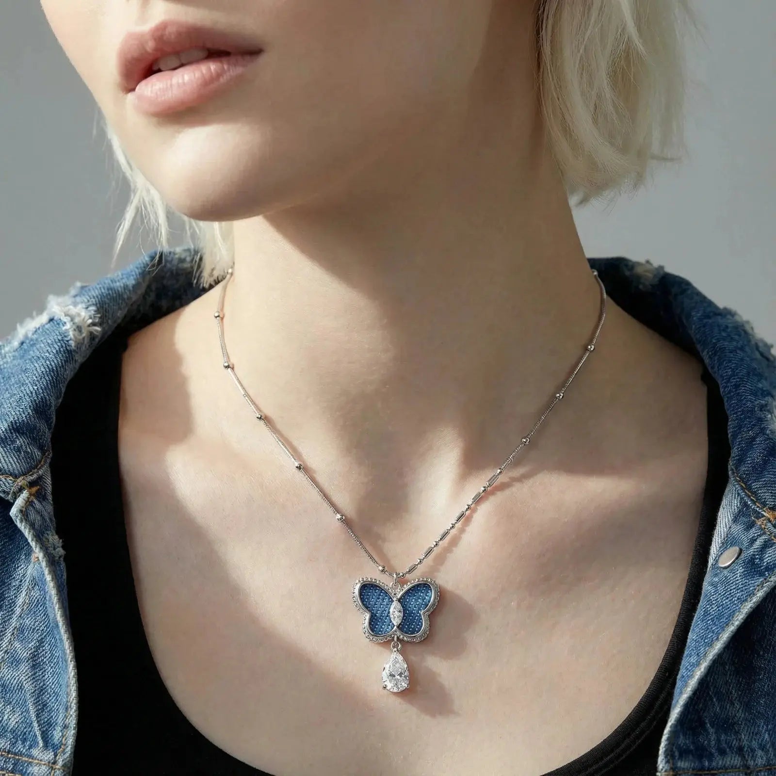 Person wearing a butterfly pendant necklace with a denim jacket