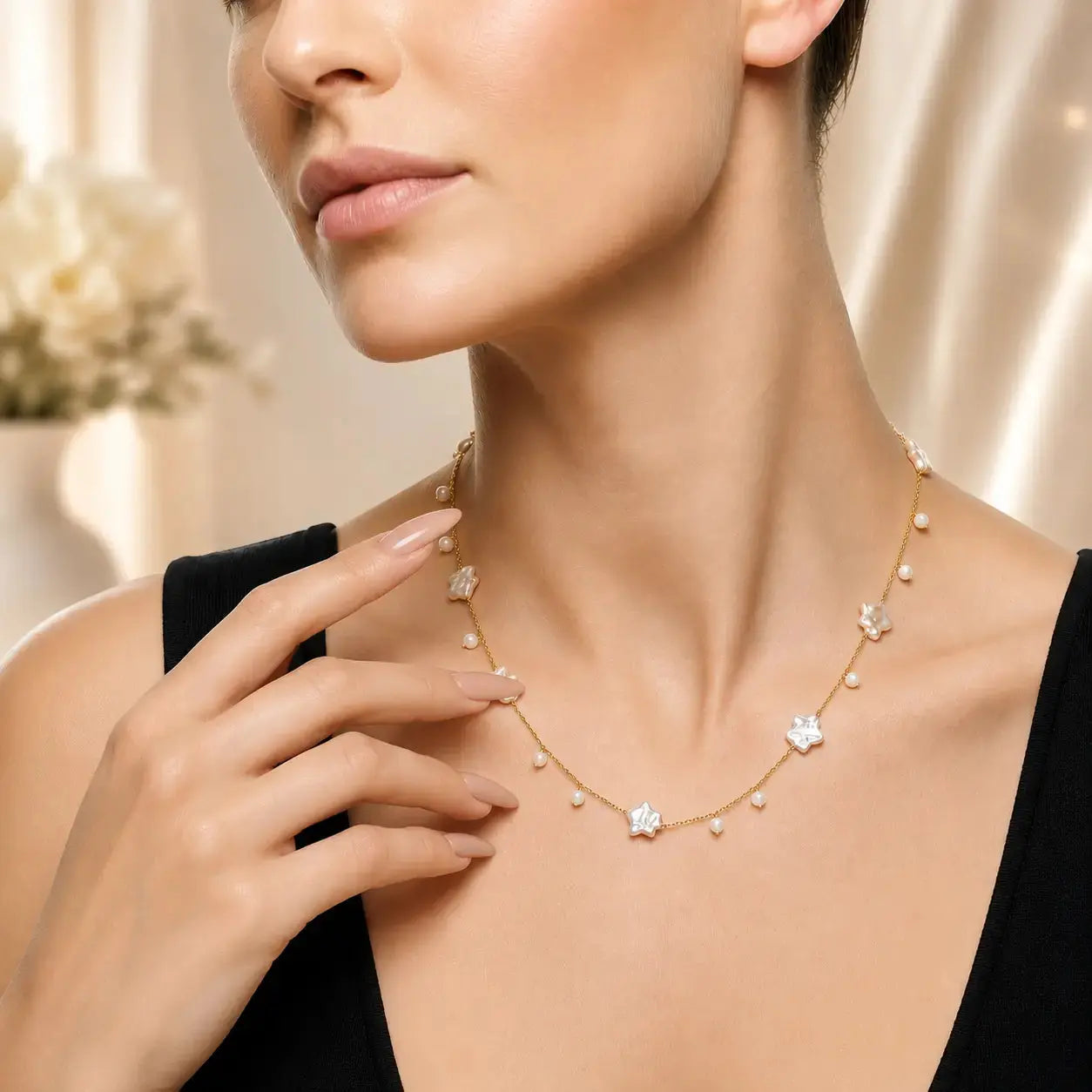 A close-up lifestyle shot of a model wearing a delicate gold necklace adorned with small white pearls and star-shaped clear crystals, styled with a black top against a soft beige background.