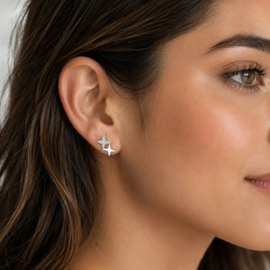 A close-up of a woman's ear wearing a small silver four-pointed star stud earring.