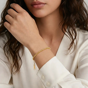 Woman wearing a gold bracelet on her wrist with a neutral background