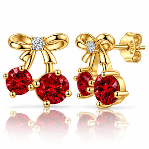 A pair of gold bow stud earrings with two round red gemstones and a small clear stone at the center, shown on a white background with reflections.