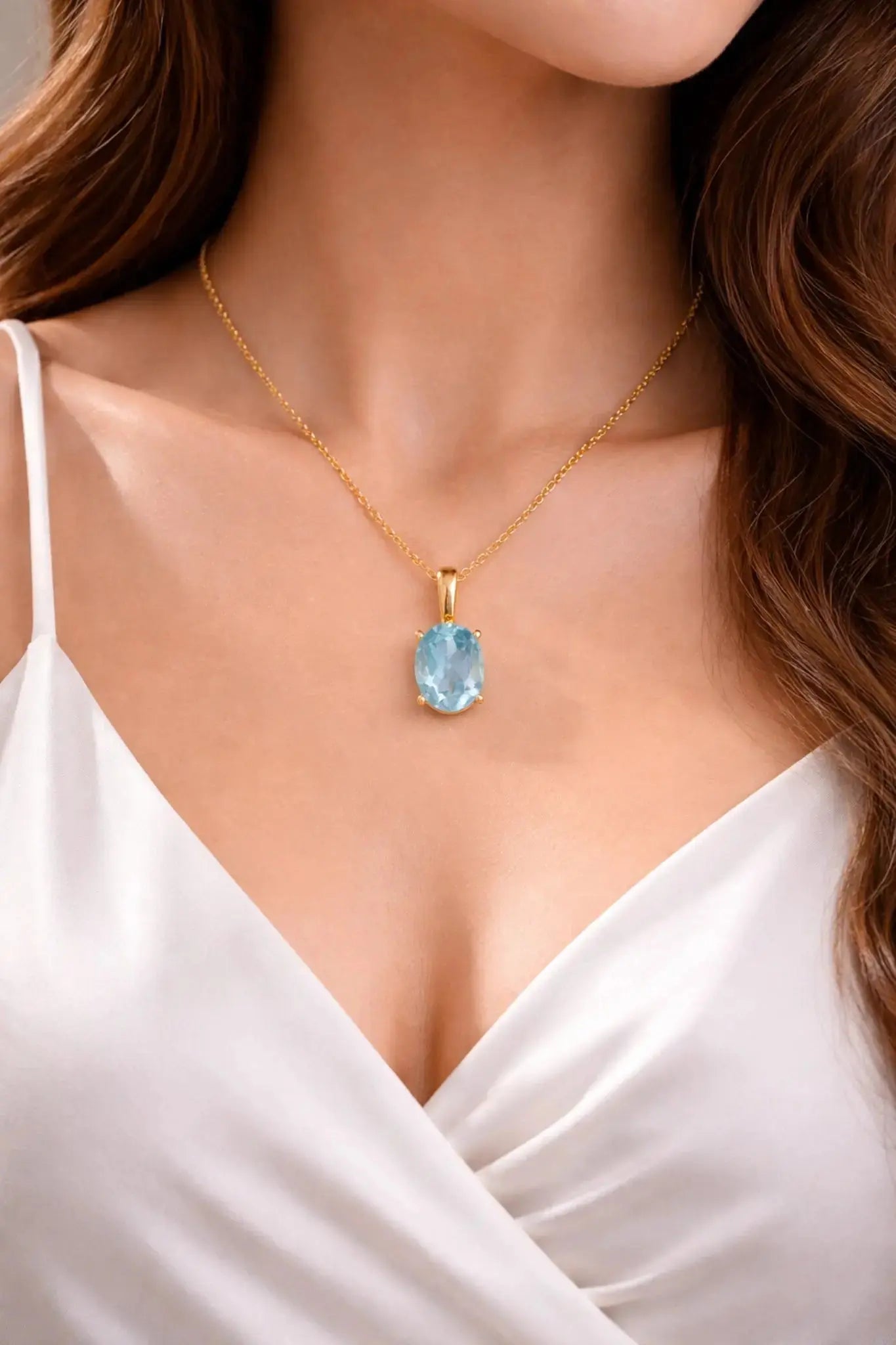 Gold necklace with a blue gemstone pendant on a model wearing a white top.