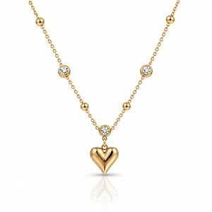 A gold necklace featuring a polished heart-shaped pendant and several small bezel-set clear stones along the chain, displayed on a clean white background with a soft reflection.
