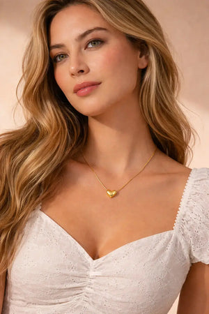 Woman wearing a gold heart-shaped necklace against a pink background