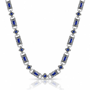 A silver-toned link necklace featuring rectangular blue gemstones and small blue floral accents, displayed on a clean white background with a soft reflection below.