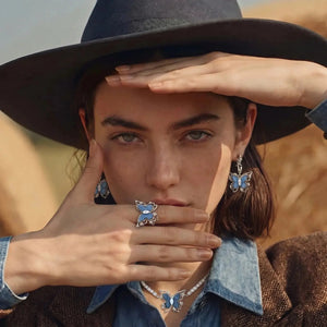 Woman wearing butterfly-themed jewelry with a hat and denim shirt in a desert setting
