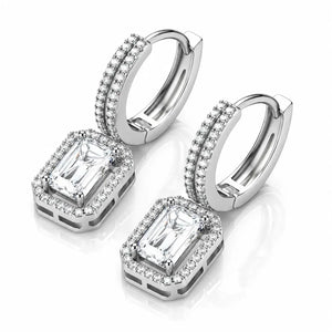 A pair of silver-toned huggie hoop earrings with rectangular emerald-cut clear stones and halo accents, displayed on a clean white background with a soft reflection.