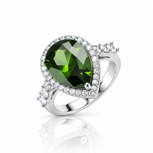 A silver ring featuring a large pear-cut green gemstone surrounded by a halo of small clear stones, with additional clear stones along the band, shown on a white background with a soft reflection.