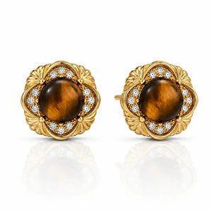 A pair of gold round stud earrings featuring a central brown tiger's eye stone surrounded by a halo of small clear stones, set in an ornate floral gold frame, on a white background with a soft reflection.