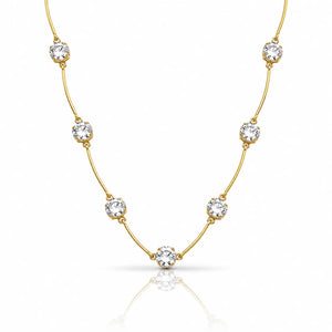 A delicate yellow gold necklace featuring seven round-cut clear gemstones spaced along the chain, displayed on a clean white background with a soft reflection below.