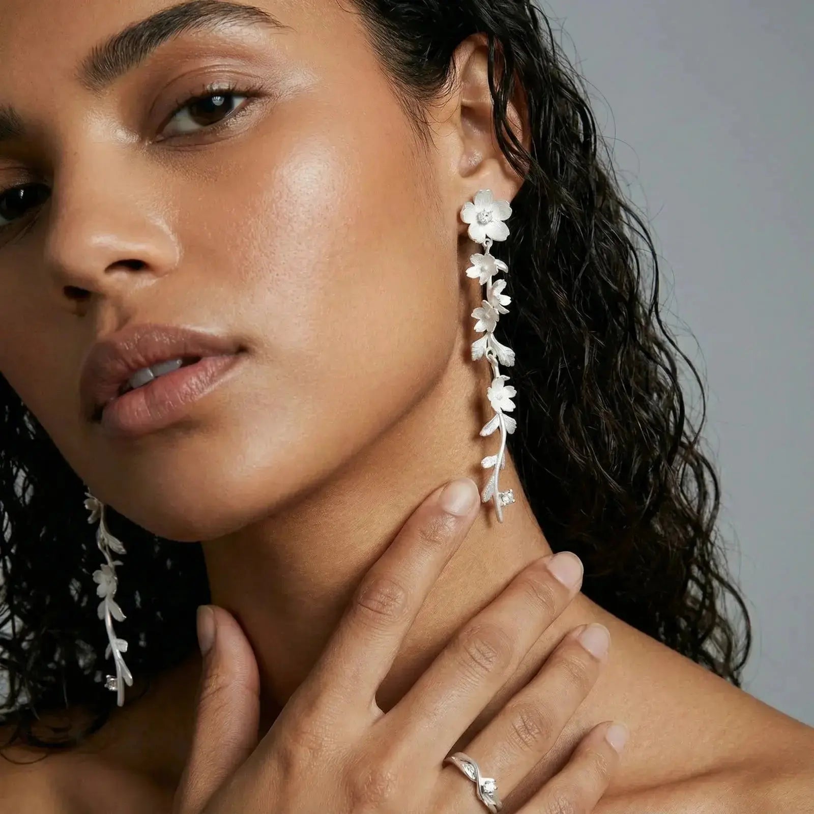 Woman wearing silver floral vine drop earrings and a delicate silver ring