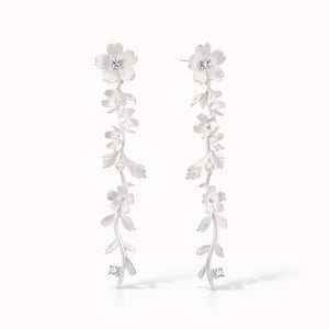 Silver drop earrings with floral and vine design and sparkling gemstone accents on white background.