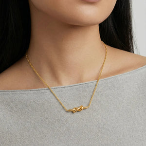 18K gold plated knot necklace on woman wearing light grey top