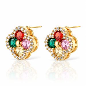 A pair of gold flower-shaped stud earrings with multicolor gemstones (red, green, pink, and yellow) surrounded by clear crystal halo details, shown on a white background with a soft reflection.