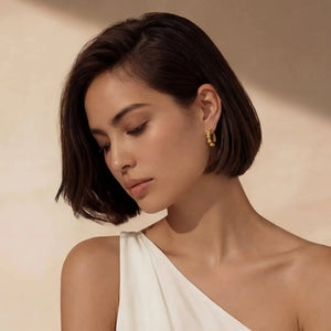 Woman wearing gold bamboo hoop earrings with an elegant white one-shoulder top