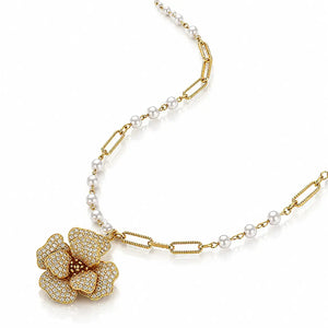 A luxury gold and pearl necklace featuring a large flower-shaped pendant paved with small clear stones, accented by a chain of white pearls and gold paperclip links, on a white background.