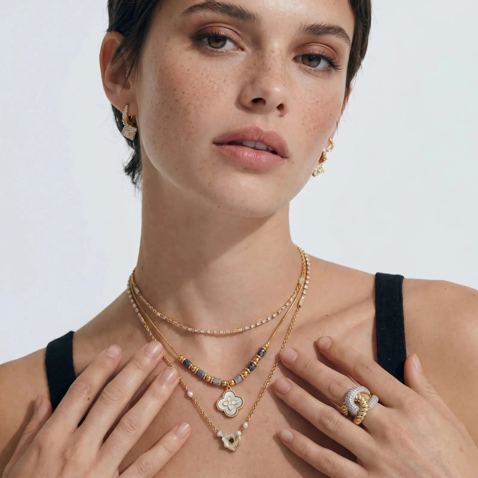Woman wearing gold necklaces and a ring on a plain background