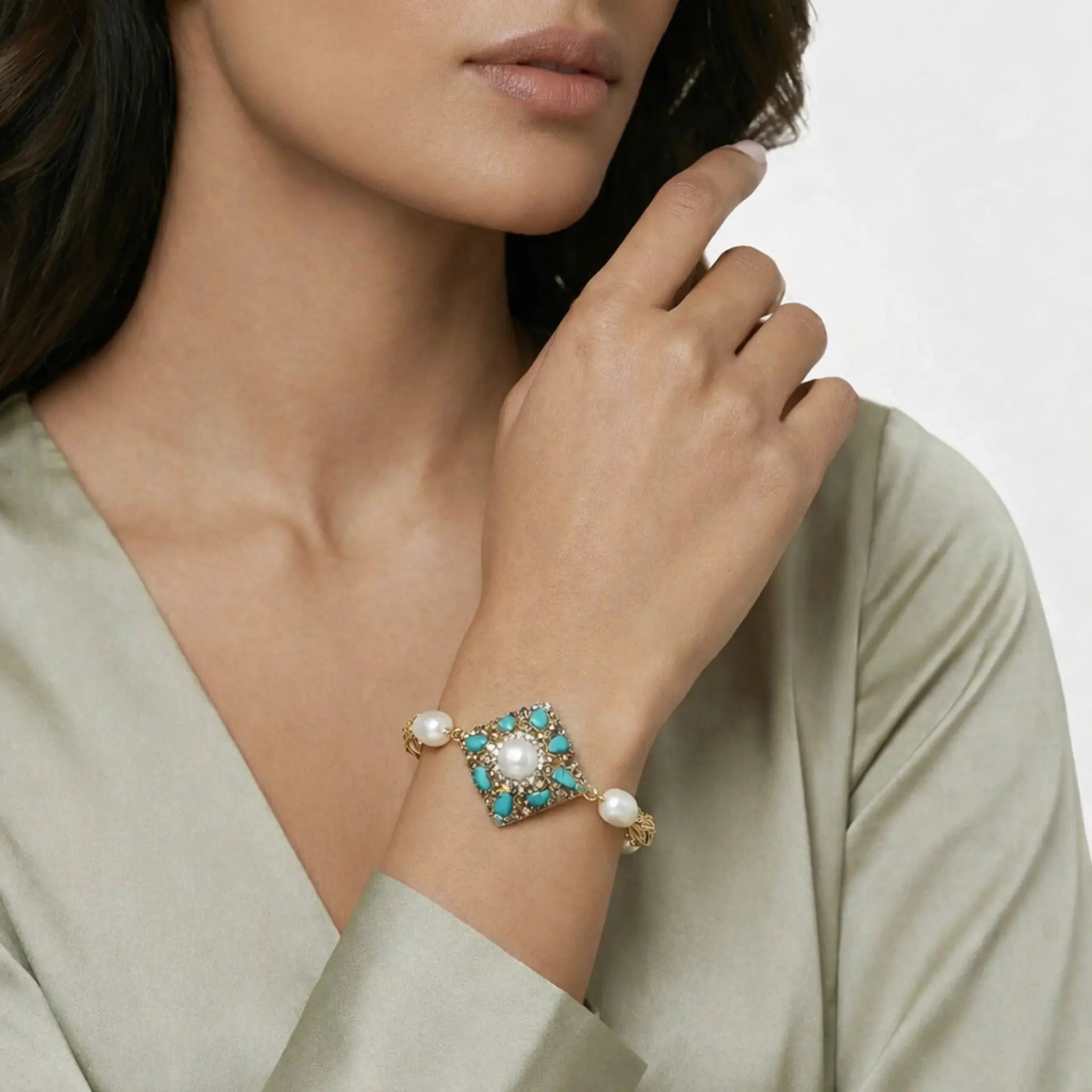Woman wearing a gold bracelet with pearls and turquoise stones, styled with an elegant outfit.