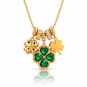 A gold St. Patrick's Day necklace featuring three shamrock charms: one large green four-leaf clover with emerald-cut stones, one solid gold shamrock, and one small gold shamrock with clear stones, on a gold ball chain.