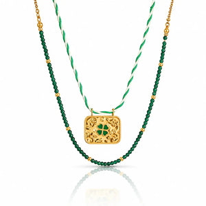 A double-strand St. Patrick's Day necklace featuring a gold filigree clover pendant and a green beaded strand layered over a white and green twisted cord chain.