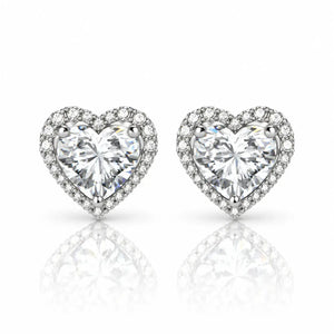 A pair of heart-shaped stud earrings featuring large clear heart-cut center stones surrounded by a halo of smaller clear stones, set in a silver-toned metal on a white background with a soft reflection below.